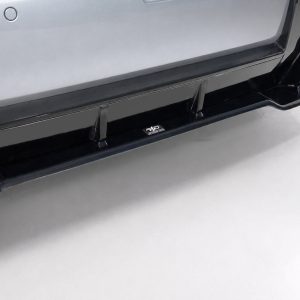 Close-up of a black running board along the bottom of a silver SUV bumper with a small emblem in the center.