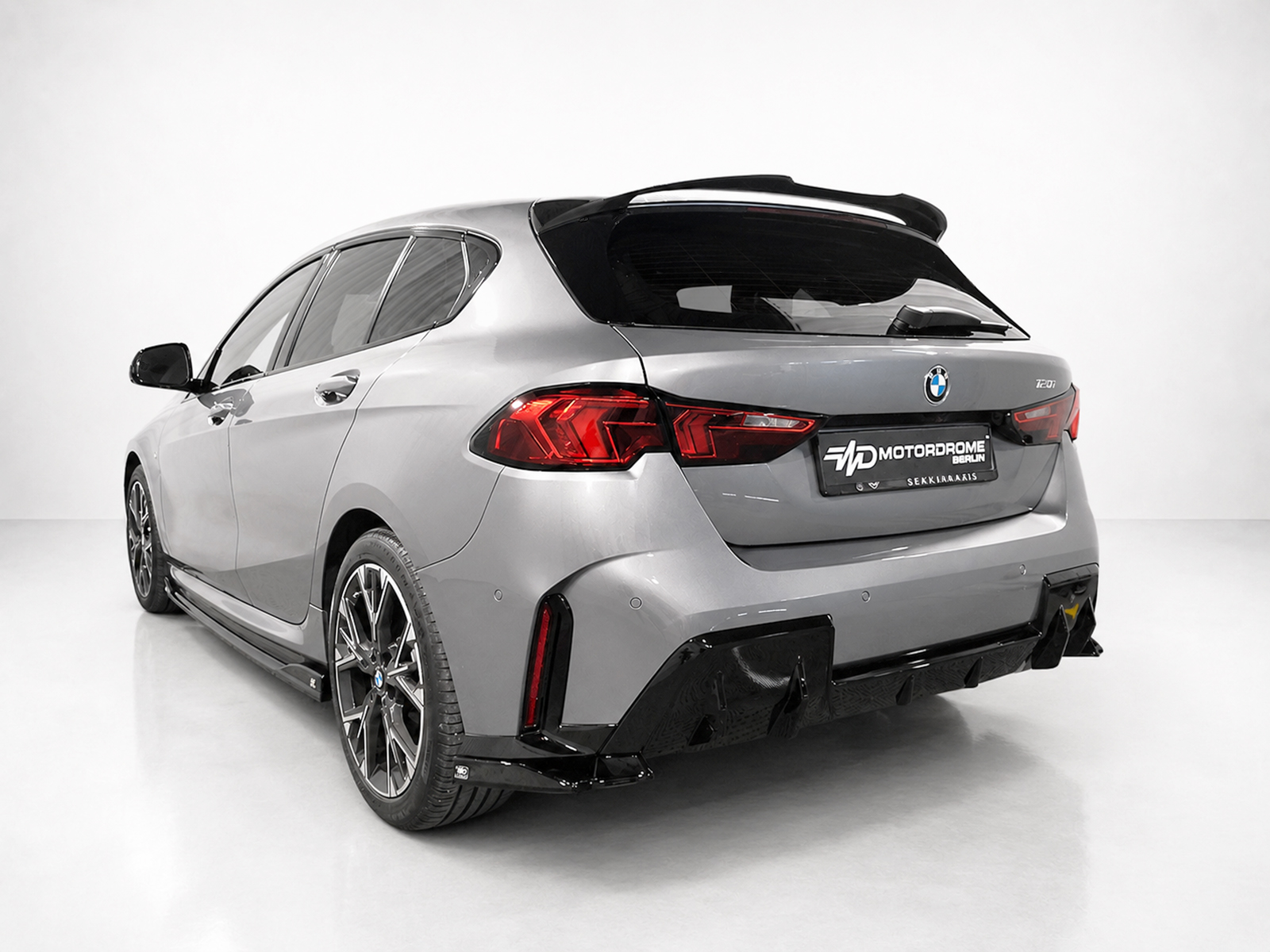 K215-006_1jpg - OPSHOLDERS Rear-left view of a silver BMW hatchback with a sports rear bumper and large alloy wheels in a studio setting, no people present.