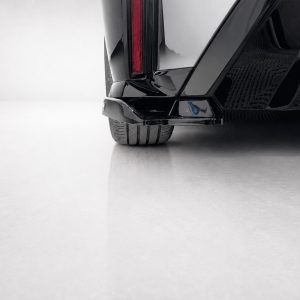 K215-006_3jpg - OPSHOLDERS Close-up of the rear corner of a shiny black car, showing the taillight and tire on a light floor surface.