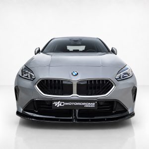 Front view of a silver BMW car with a large black grille and MotorDrome Design license plate in a studio setting