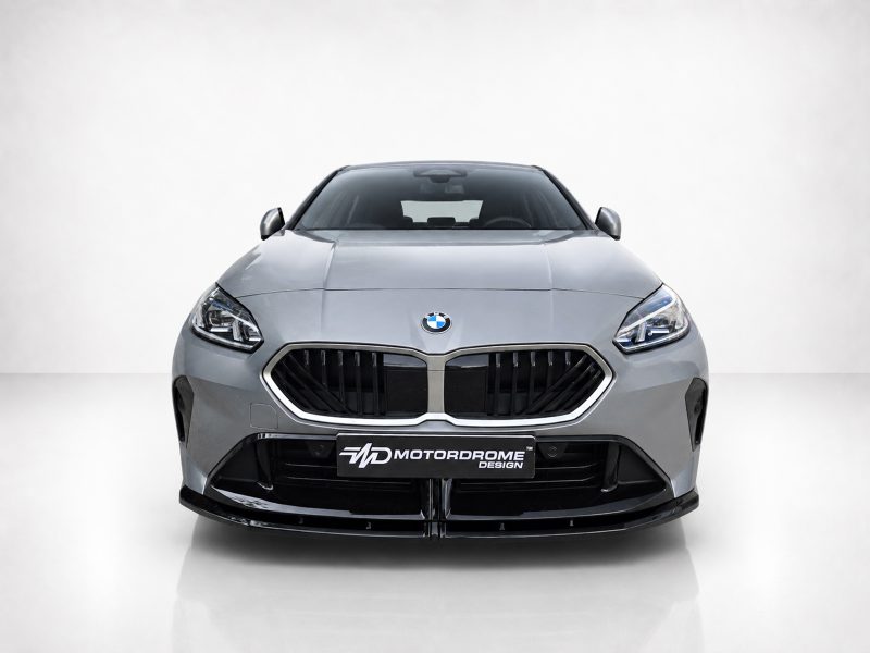 Front view of a silver BMW car with a large black grille and MotorDrome Design license plate in a studio setting