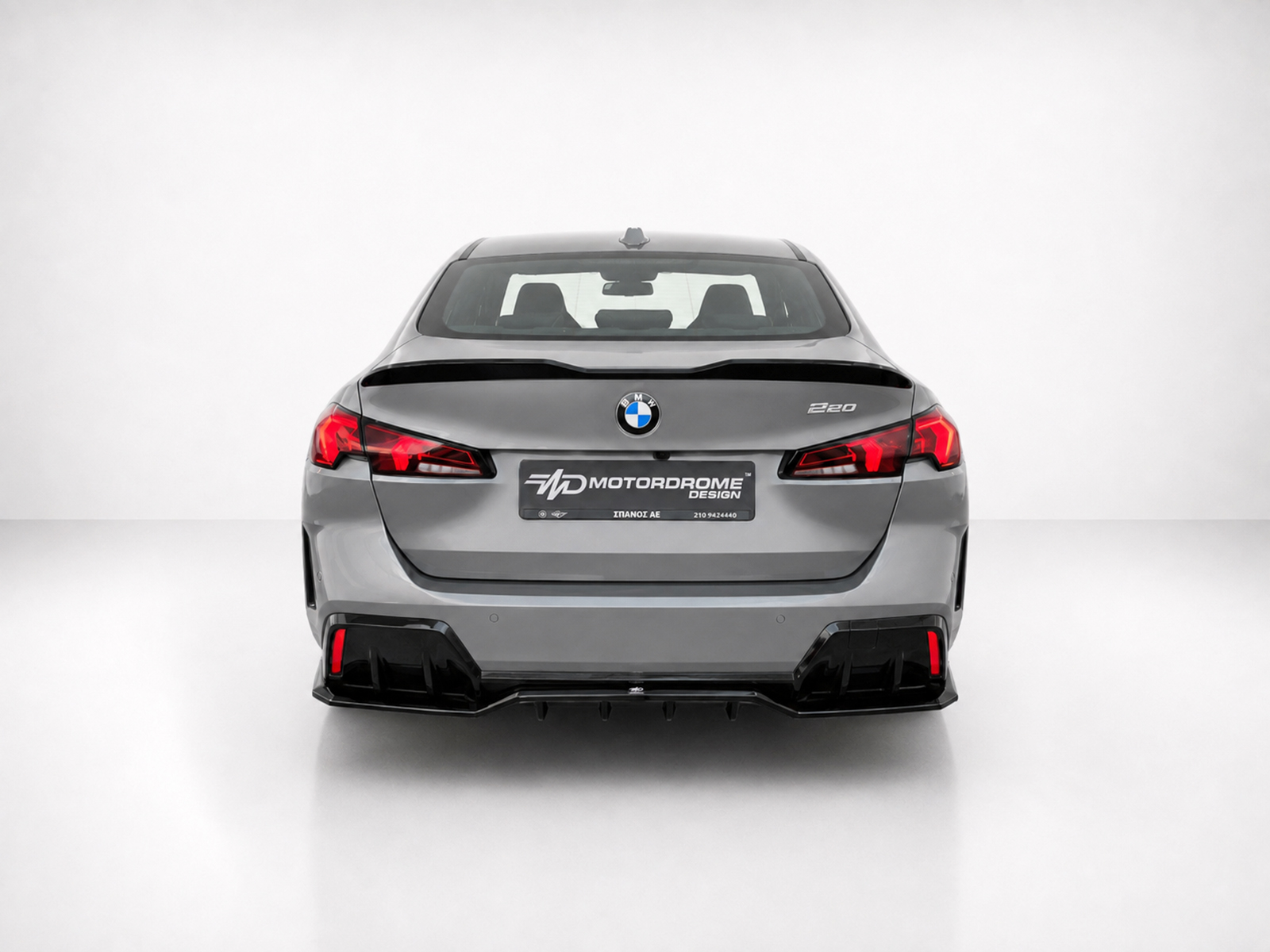 K215-008_1jpg - OPSHOLDERS Rear view of a gray BMW 220 in a white studio, with red taillights and a showroom MD MotorDrome plate
