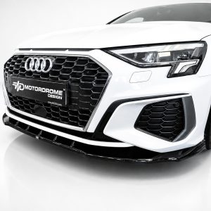 Front view of a white Audi car in a studio, showing the black honeycomb grille and prominent headlights with a MotorDrome Design plate on the bumper.