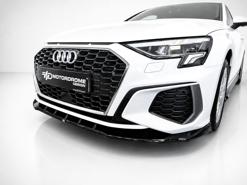Front view of a white Audi car in a studio, showing the black honeycomb grille and prominent headlights with a MotorDrome Design plate on the bumper.