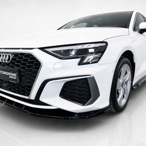 White Audi sedan shown from a front-three-quarter angle with a large black honeycomb grille and LED headlights, on a light backdrop.
