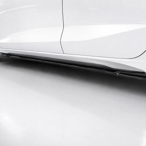 Close-up of a white car's lower side panel and side skirt, with a chrome trim and visible wheel on the left.