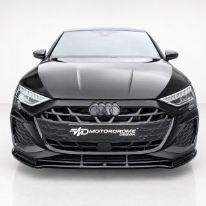 Front view of a glossy black Audi car facing the camera in a bright studio, with the four-ring logo on the grille and a Motordrome Design plate nearby.