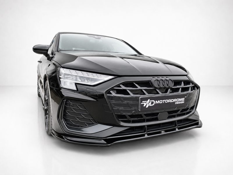 Black Audi at a three-quarter front view in a white studio, showing sleek grille and headlights with a Motordrome Design plate