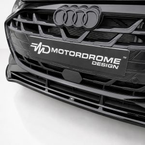 Close-up of a black Audi front grille with the four-ring logo and a Motordrome Design plate in the center, glossy chrome accents evident.