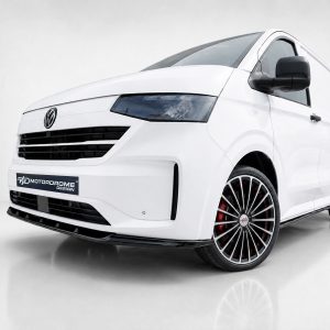 Front three-quarter view of a white Volkswagen van with black front grille and red-accent wheels, displayed in a showroom setting, logo plate reads 'Motordrome Design'
