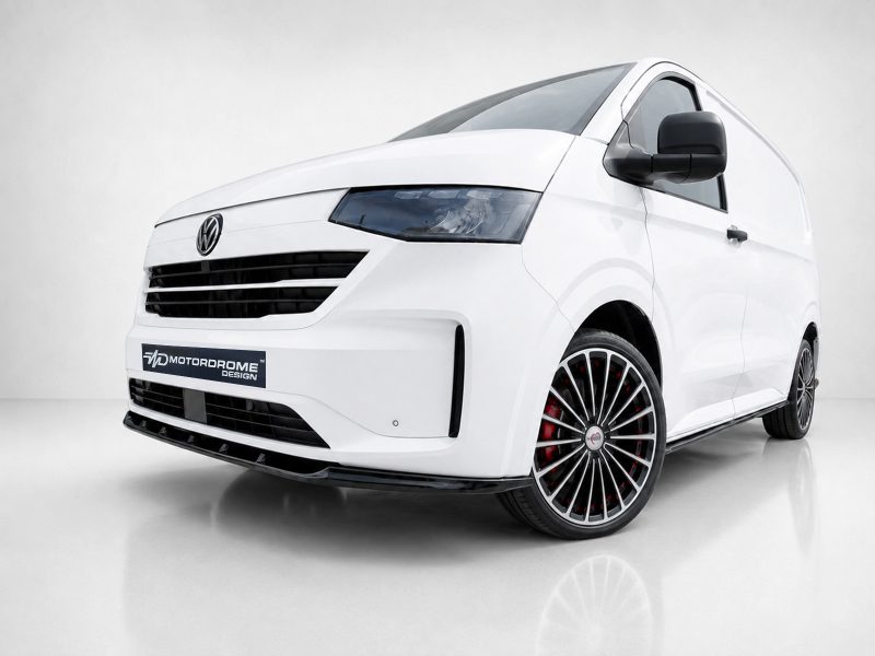 Front three-quarter view of a white Volkswagen van with black front grille and red-accent wheels, displayed in a showroom setting, logo plate reads 'Motordrome Design'