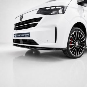 Close-up of a white car's front end showing a black grille, a MotorDrome Design plate, and a multi-spoke wheel with red brake calipers.