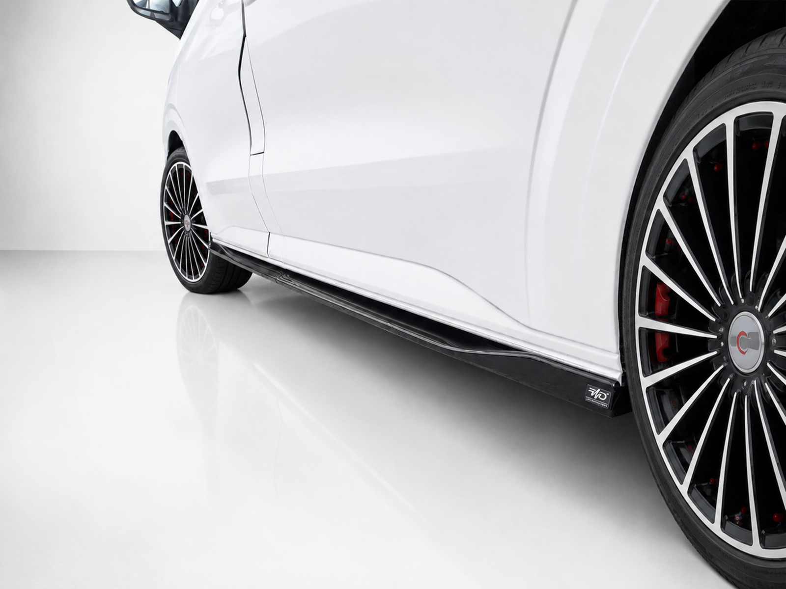 K217-004_2jpg - OPSHOLDERS Close-up of a white car’s side with a large multi-spoke alloy wheel and red brake calipers visible through the rim.
