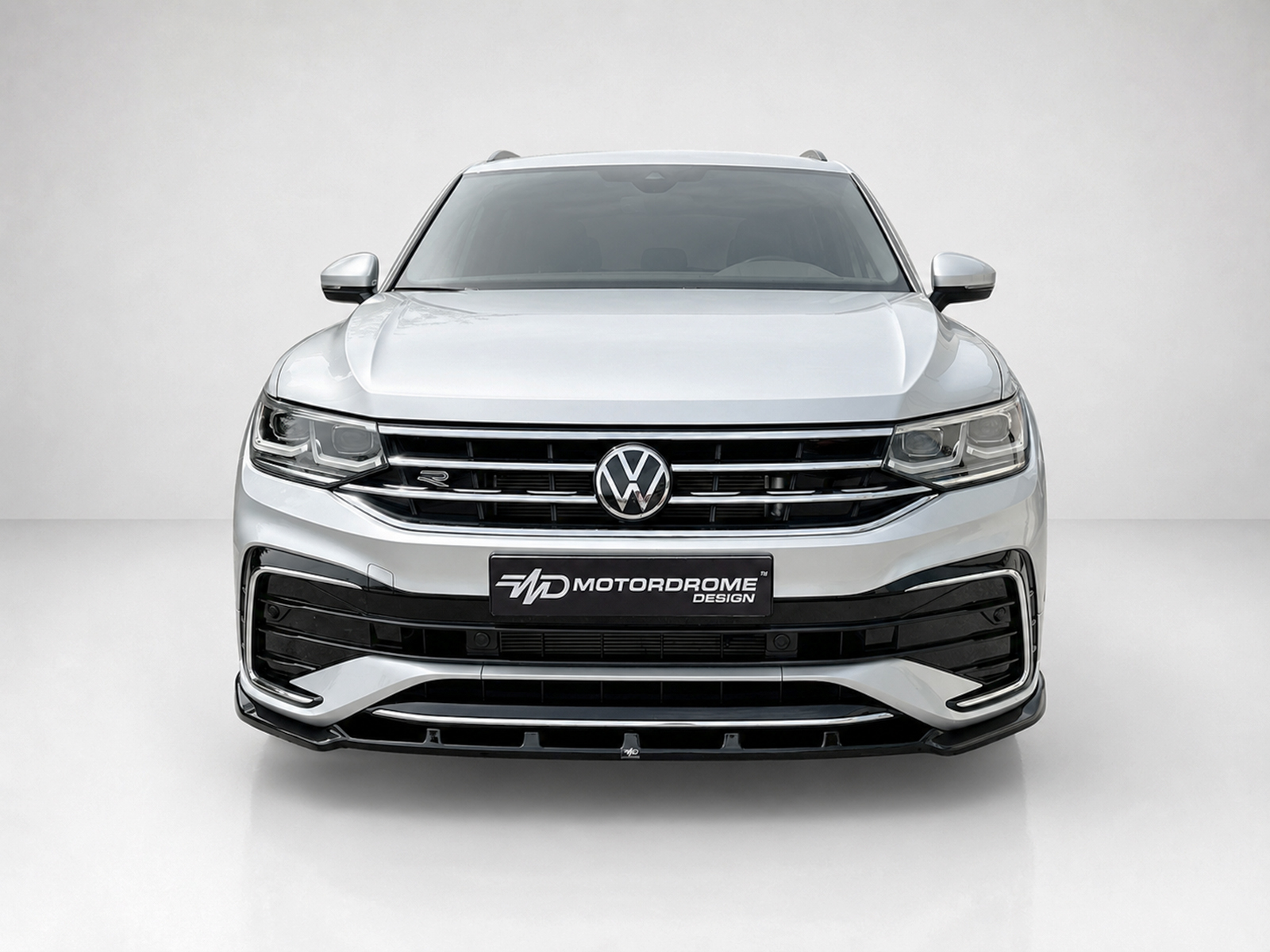 K218-001_1jpg - OPSHOLDERS Front view of a silver Volkswagen SUV with a chrome grille and VW emblem, indoors on a light background.