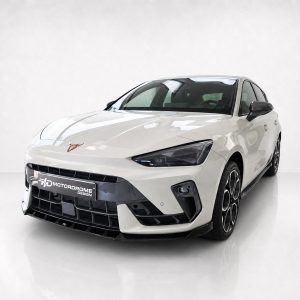 White sports sedan in a studio, angled front view with black grille and Motordrome Design license plate.