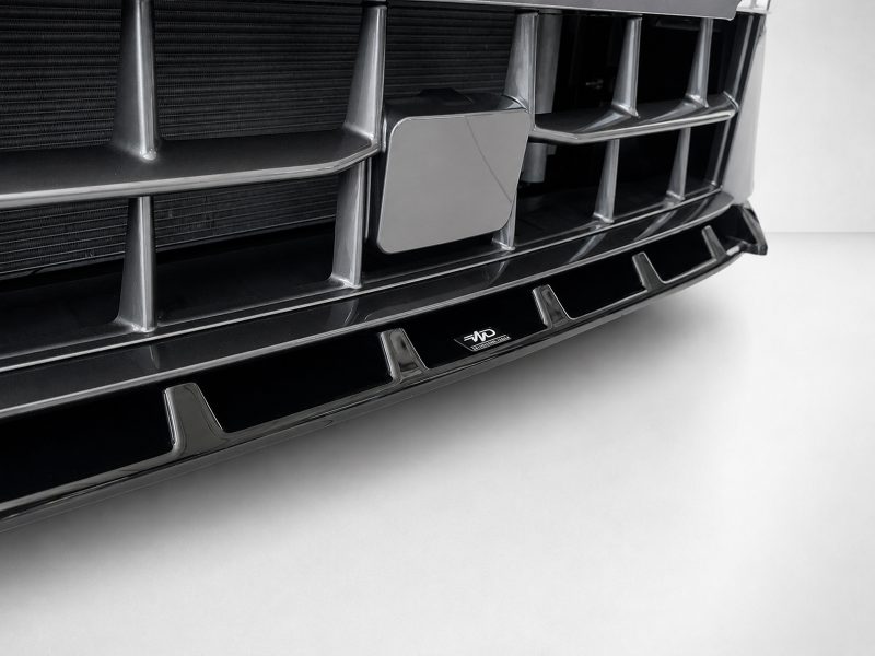 Close-up of a glossy black car front grille with chrome vertical bars and a central rectangular emblem, photographed from a low angle.