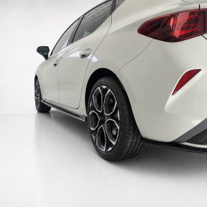 White car shown from the rear-side, featuring a prominent red taillight and intricate black-silver alloy wheel design.