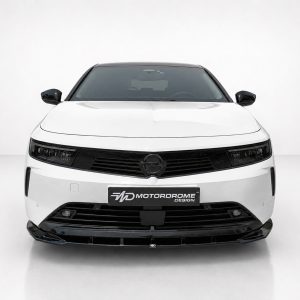Front view of a white car facing the camera, with a black grille and glossy bumper, displaying a Motordrome Design plate.
