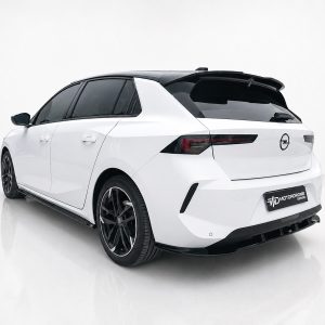 Rear-left three-quarter view of a white hatchback with a black roof spoiler in a bright studio. Dark tinted windows and large black alloy wheels visible.