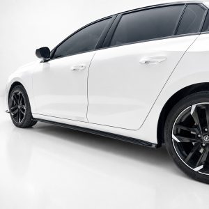 White car photographed from the side in a studio, showing glossy body, black alloy wheels, and tinted windows on a sleek sedan example.