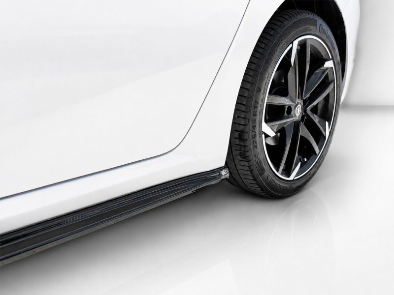 Close-up of a white car's rear wheel and glossy black alloy rim, with a low side skirt visible beneath the door panel.