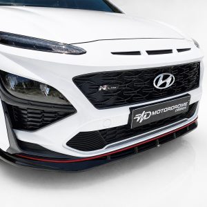 Front angle of a white Hyundai with black honeycomb grille, N Line badge, and sporty lower splitter with red accents.