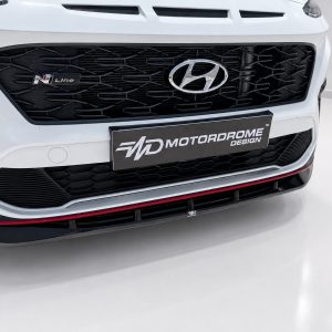 Close-up of a white Hyundai front with a black mesh grille, Hyundai emblem, and an MOTORDROME DESIGN license plate.