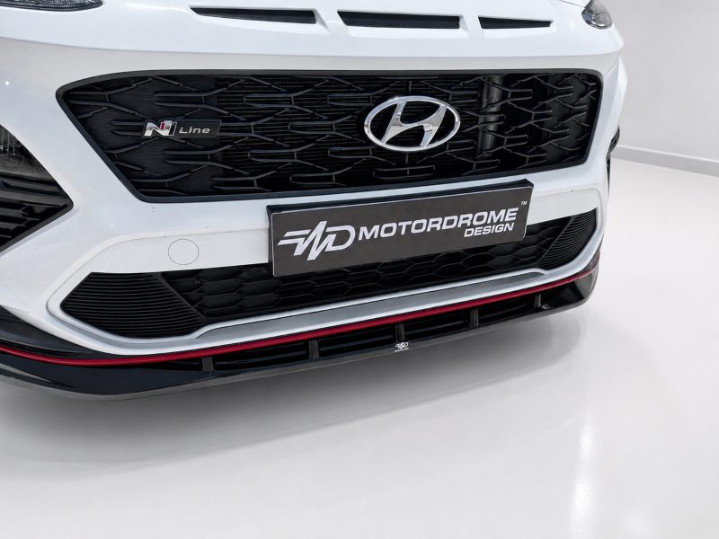 Close-up of a white Hyundai front with a black mesh grille, Hyundai emblem, and an MOTORDROME DESIGN license plate.