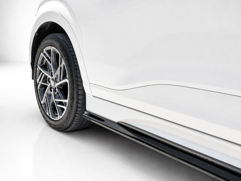 Close-up of a white car's alloy wheel and lower body panel in a studio setting.