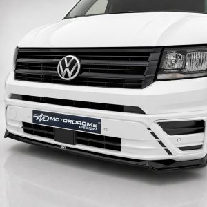 Front view of a white Volkswagen van with a black grille, VW emblem, and a Motordrome Design plate on the bumper coolly showcased in a studio setting.