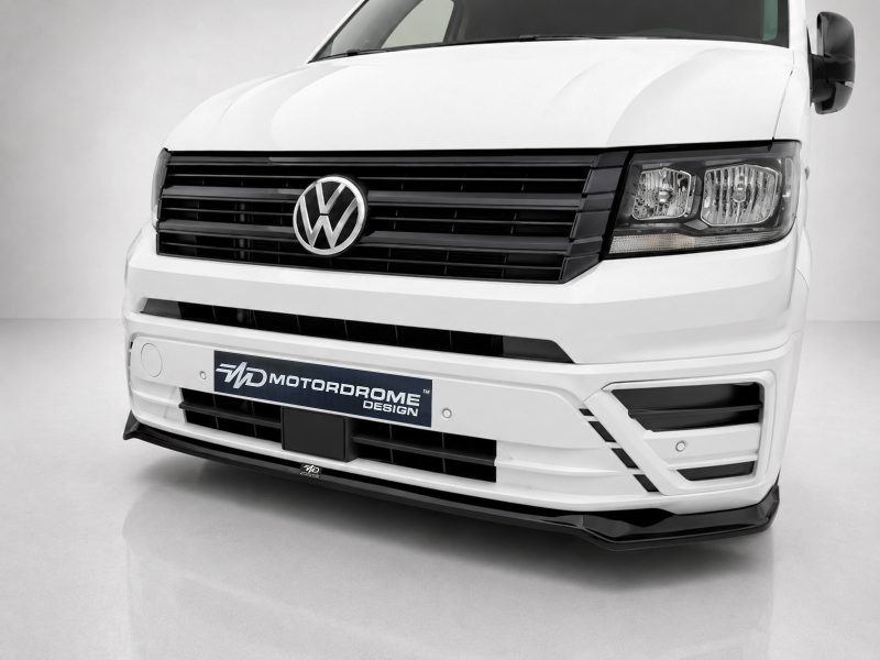 Front view of a white Volkswagen van with a black grille, VW emblem, and a Motordrome Design plate on the bumper coolly showcased in a studio setting.