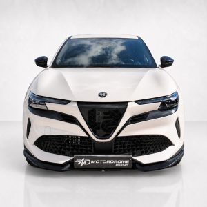 Front view of a white Alfa Romeo SUV with a large black grille and sleek headlights, parked indoors.