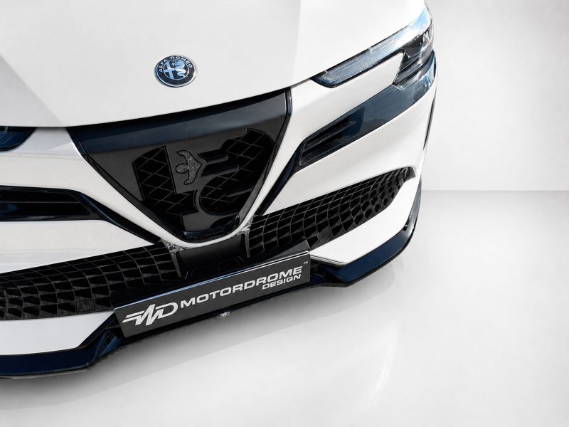 Close-up of a white car front showing the Alfa Romeo badge, sleek headlight, and black mesh grille.