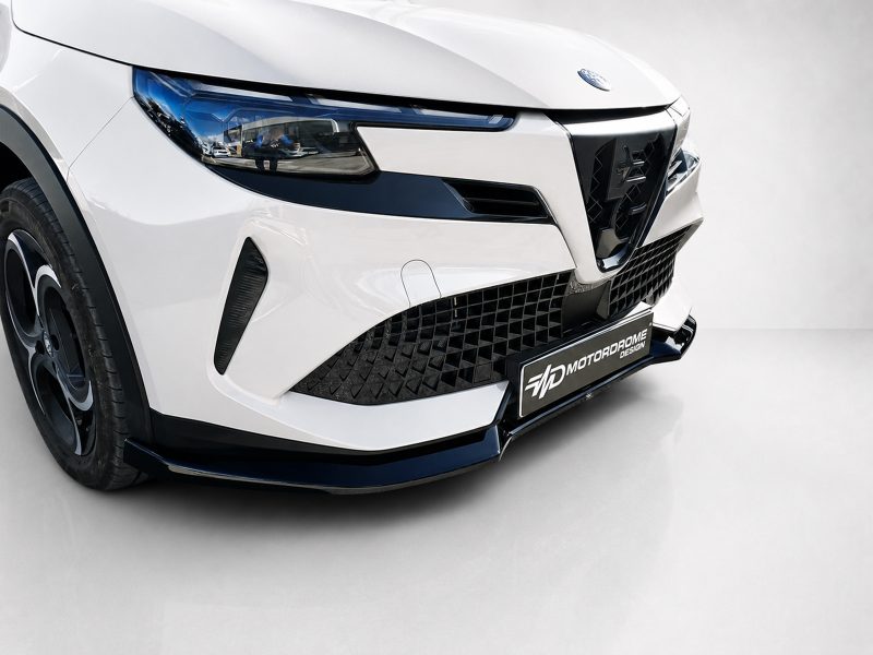 Close-up of a white modern car front, showing a black mesh grille, angular headlight with blue accents, and a front splitter.