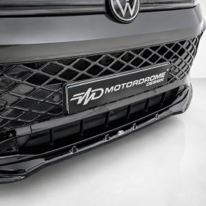 K228-001_5jpg - OPSHOLDERS Close-up of a black car's front end showing a diamond-pattern grille and a Motorodrome Design license plate in the center.
