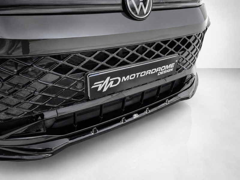 K228-001_5jpg - OPSHOLDERS Close-up of a black car's front end showing a diamond-pattern grille and a Motorodrome Design license plate in the center.