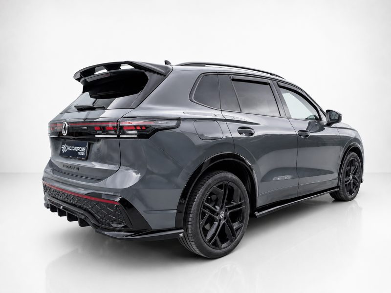 Rear three-quarter view of a dark gray Volkswagen Tiguan with black wheels in a bright studio setting