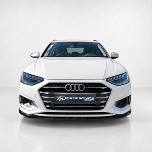 Front view of a white Audi sedan in a studio, with the Motordrome Design license plate visible on the grille.
