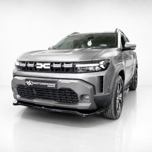 Front-right angled view of a silver pickup truck in a bright studio, highlighting its bold grille and rugged bumper with a Motordrome Design plate in the foreground.