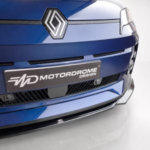 Close-up of a blue car's front end showing the Renault-style diamond badge and a 'Motordrome Design' license plate