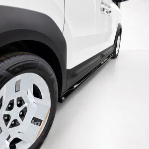 Close-up of a white SUV's front wheel and side running board in a bright studio, showing tire tread and black rocker panel.