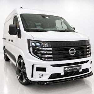 Front three-quarter view of a white Nissan Interstar van with a black grille and large alloy wheels in a studio setting.