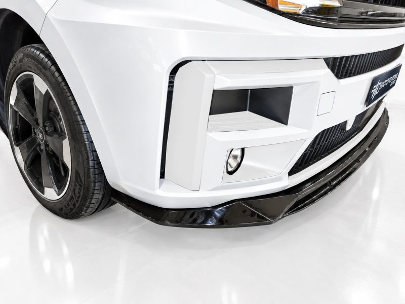 Close-up of a white car front with a large black front splitter, angular bumper details, and a wheel visible on the left
