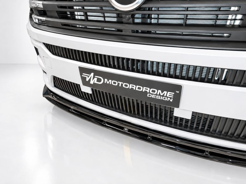Front view of a white vehicle’s grille with a black 'Motordome Design' plate.