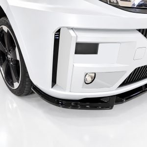 Close-up of a white car's front end, showing the bumper, grille, fog light, and a large black alloy wheel with the Audi emblem visible on the rim