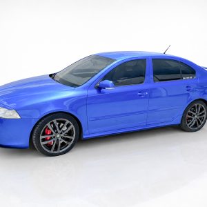 Blue sports sedan photographed from a front-left angle, showing large black alloy wheels with red brake calipers and a rear spoiler.