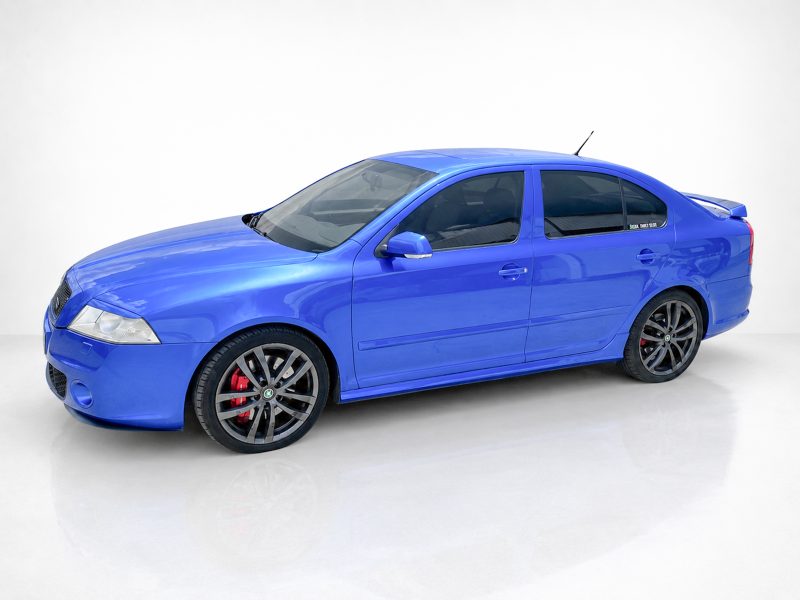 Blue sports sedan photographed from a front-left angle, showing large black alloy wheels with red brake calipers and a rear spoiler.