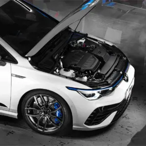 R600-EVO-1webp - OPSHOLDERS White sports car with hood opened, exposing engine and blue brake calipers in a garage scene