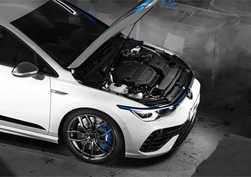 R600-EVO-1webp - OPSHOLDERS White sports car with hood opened, exposing engine and blue brake calipers in a garage scene