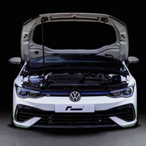Front view of a white Volkswagen with its hood open, exposing the engine against a black background